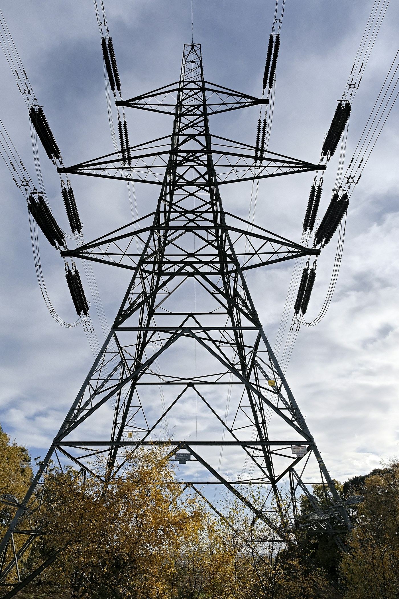 Electricity transmission tower against a grey storm sky, representing the power grid infrastructure covered by parametric insurance