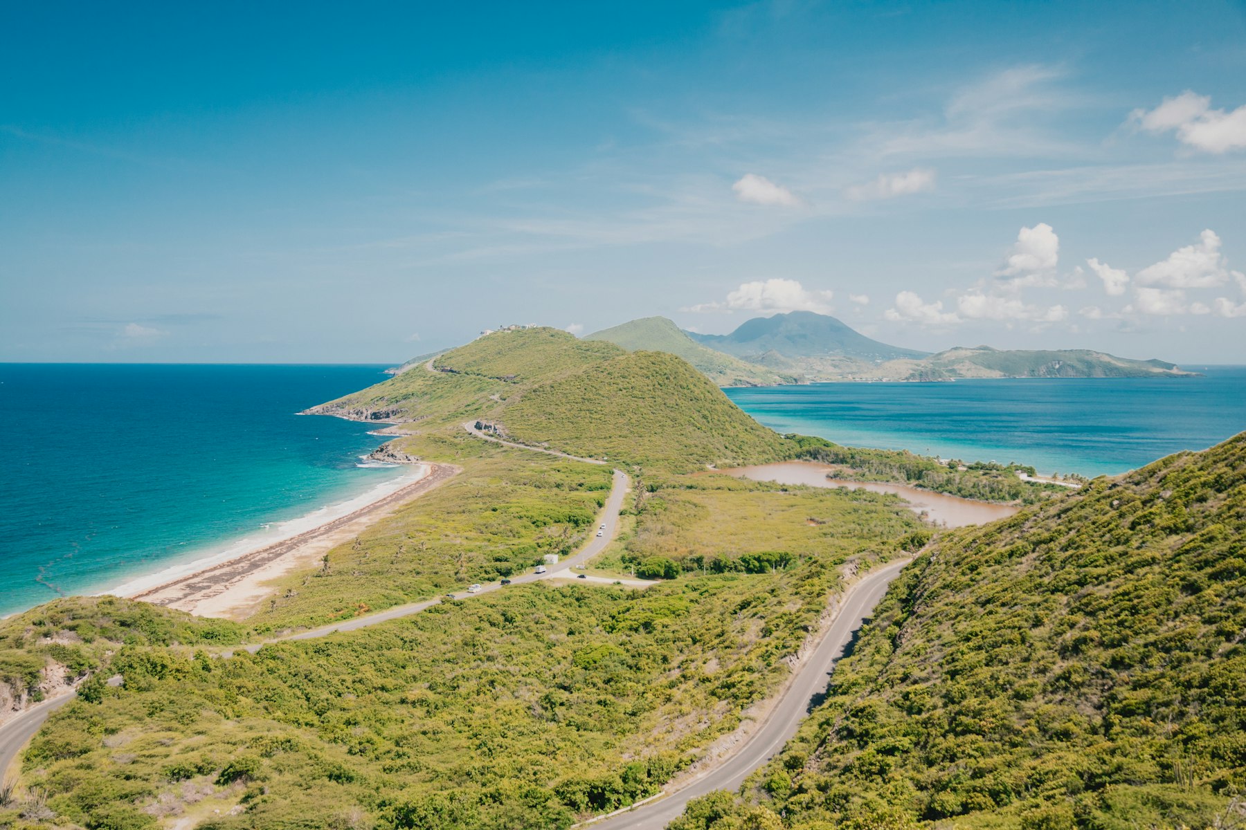 Winding roads, green hills and a sandy coast with distant mountains, photographed in Saint Kitts and Nevis